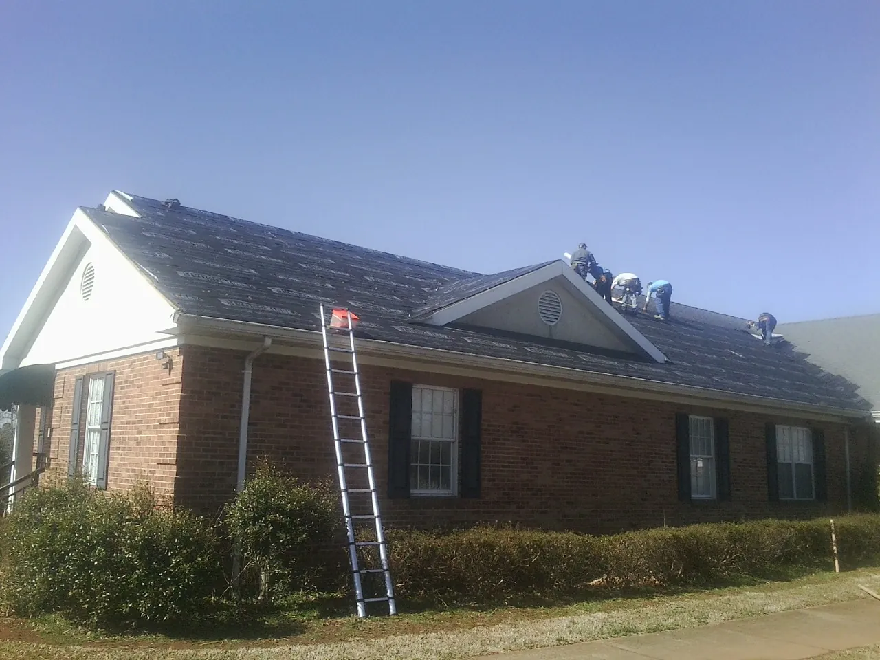 Crew tearing shingles off a brick ranch roof with a ladder set — Emergency Roof Repair work by our crew in Emmaus