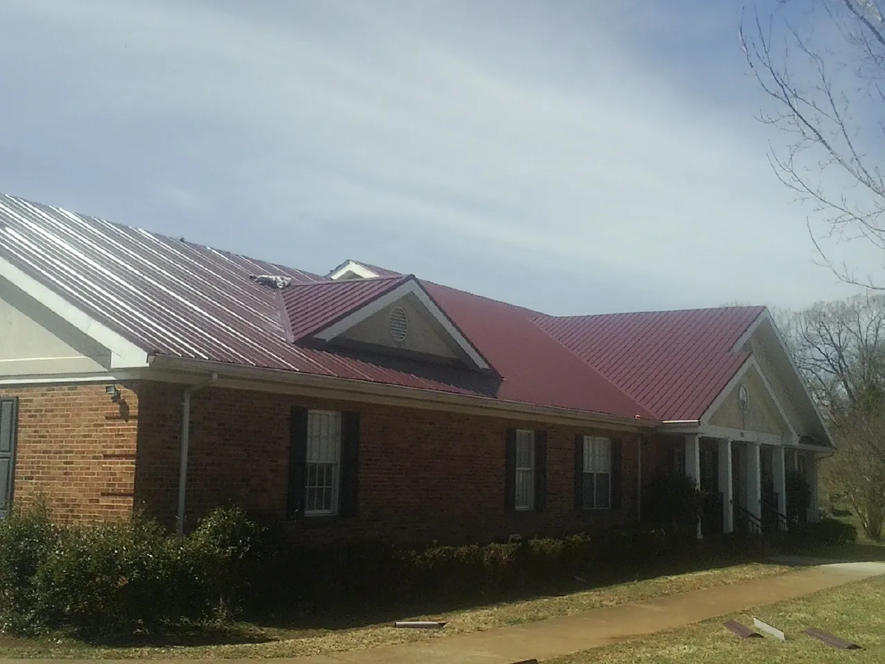 Red metal roof with gabled entries on a long brick building, from a Hail Damage Roof Repair job in Emmaus