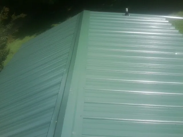New green metal panels meeting at the ridge of a roof — Flat Roof Repair work by our crew in Emmaus