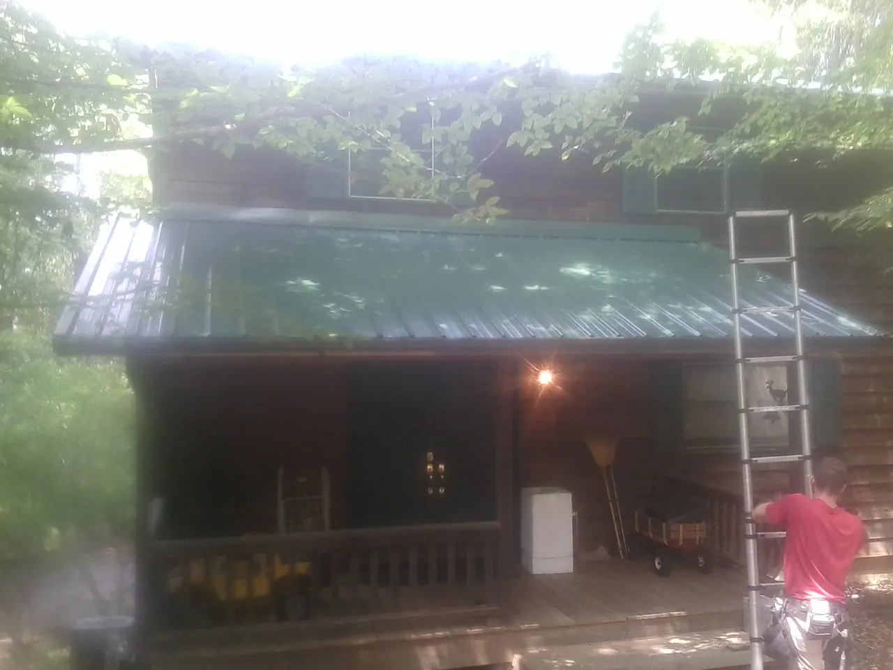 Worker on a ladder at the green porch roof of a wooded cabin in Emmaus