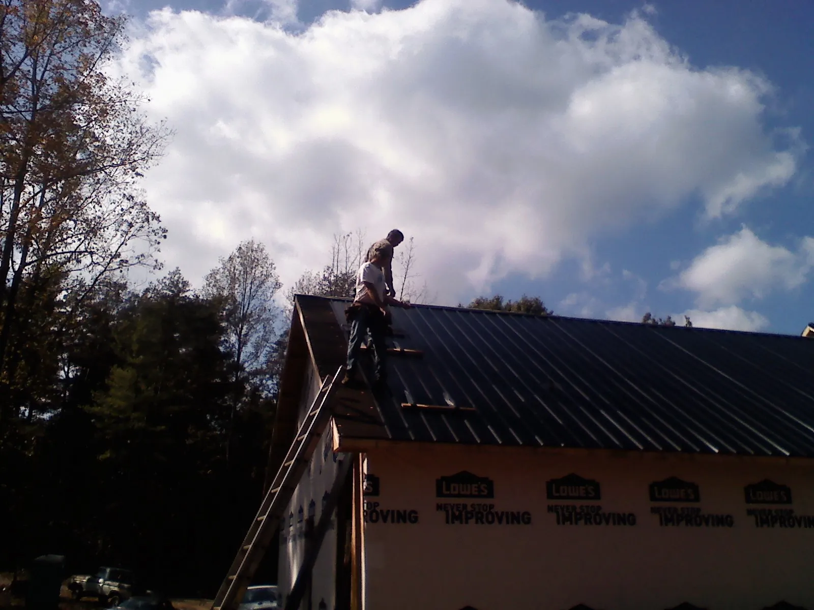 Roofer fastening dark metal panels high against a cloudy sky, from a Roof Inspection job in Emmaus
