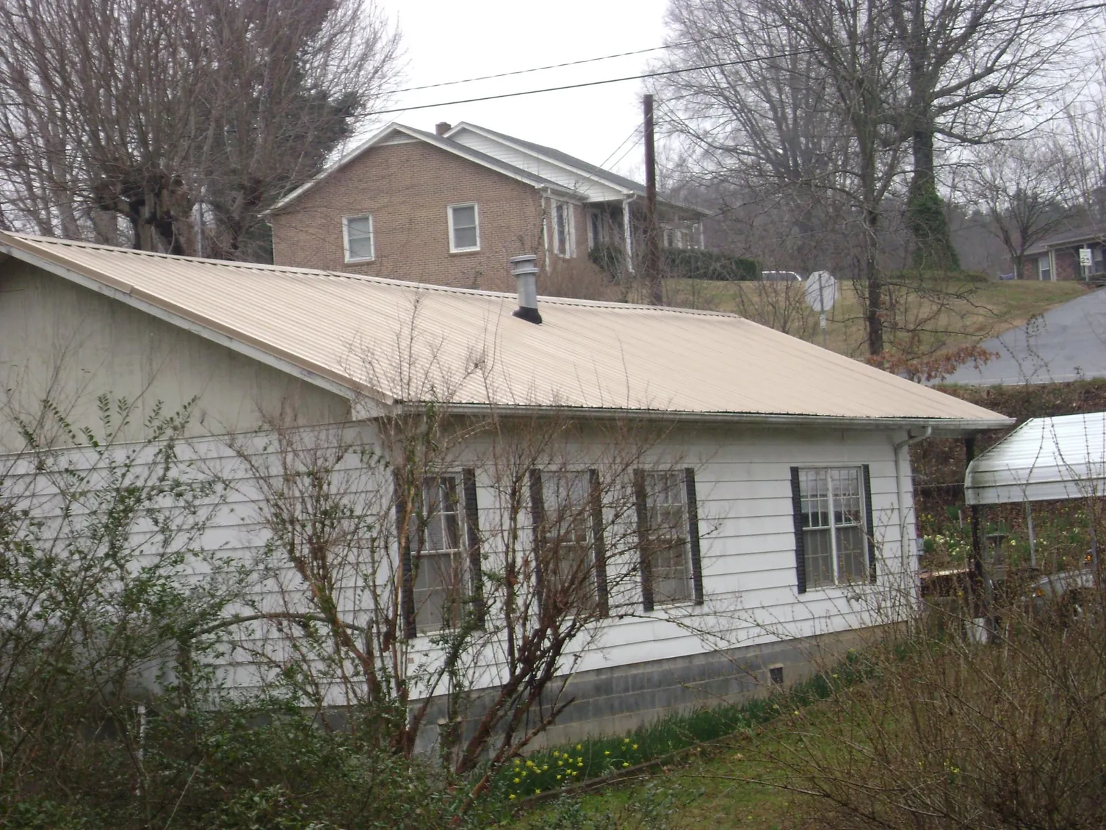 Tan metal roof on a white sided house set into a hillside — Commercial Roofing by Roofing Brothers in Emmaus